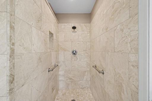 The walk-in shower features: marble floor & walls, grab bars, a product niche, and recessed lights. The walls & trim were repainted in 2024.