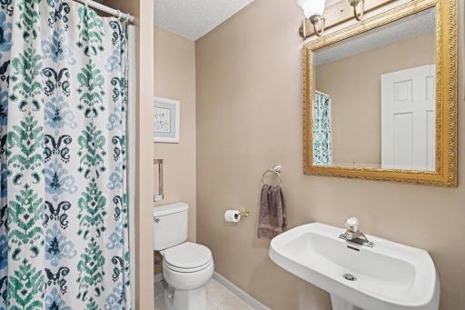 The main floor 3/4 guest bathroom features: painted walls & trim (2024), ceramic tile flooring, a pedestal sink, updated toilet, shower stall, and an exhaust fan.