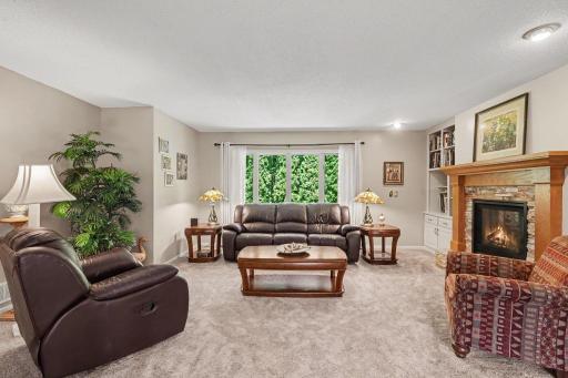 This welcoming living room features: updated carpet (2019), painted walls & trim (2024), a double-sided gas fireplace, and a large, north-facing picture window overlooking the private backyard.