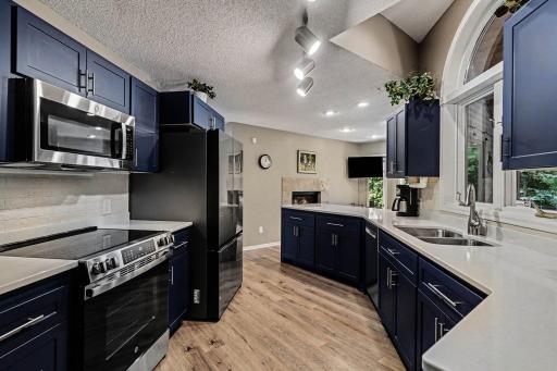 The updated kitchen features: painted walls & trim (2024), brushed nickels cabinet pulls, stainless steel appliances, a large window overlooking the screened porch, a stainless steel under-mounted sink w/brushed nickel faucet & track lighting.