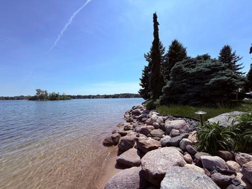 Sandy shoreline with large rip rap boulders and mature landscaping
