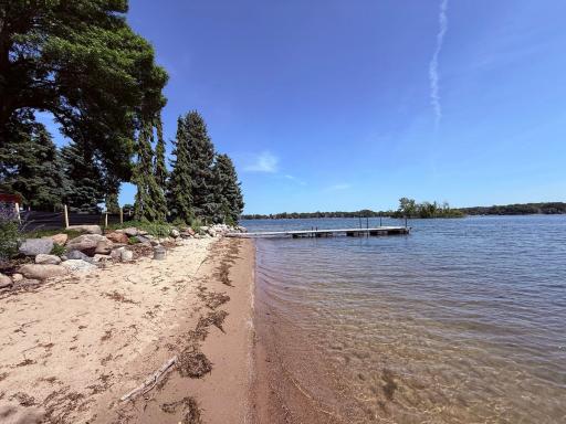 Sandy shoreline with large rip rap boulders and mature landscaping