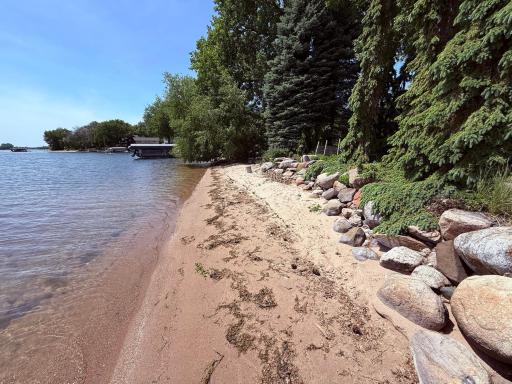Sandy shoreline with large rip rap boulders and mature landscaping