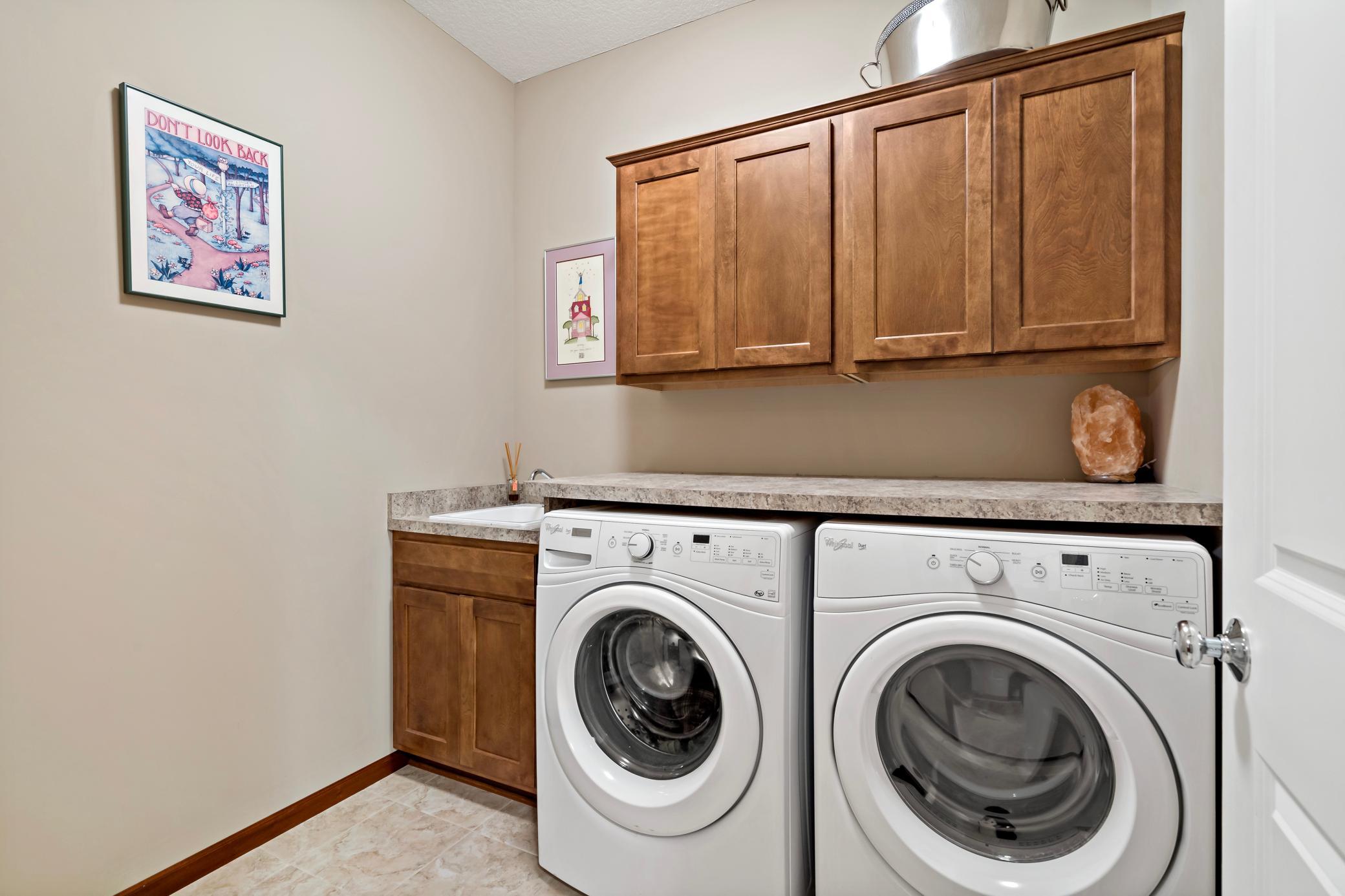 Main level laundry room is a critical and beneficial feature of "One level living". This laundry room is located near the garage access and offers a folding counter, abundant storage, and a utility sink.