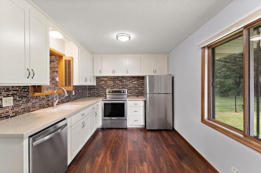 The kitchen features stainless steel appliances, including an electric stove, hardwood flooring, a large window to the backyard on the right and the pass-through to the living room is located above the kitchen sink on the left.