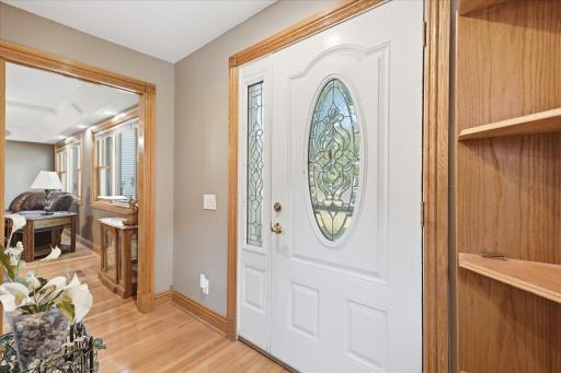 Bright and inviting foyer showcases a beautiful decorative glass entry door with matching sidelight, warm hardwood flooring, and rich natural custom wood trim.