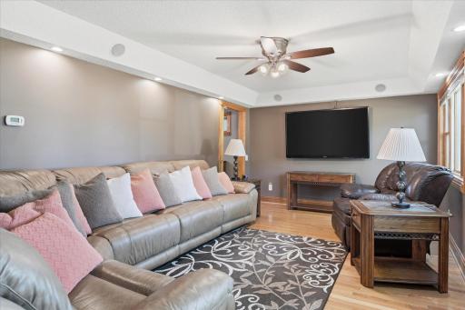 Spacious living room offers an open, comfortable gathering space with gleaming hardwood floors, recessed lighting, a ceiling fan, built-in surround sound speakers, and a custom media closet designed to keep electronics neatly organized.