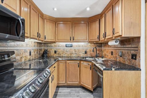 Thoughtfully designed U-shaped kitchen offers expansive granite countertops, ample meal prep space, recessed lighting, and a large pantry complete with convenient roll-out shelving for effortless organization.