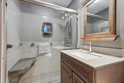 Beautifully updated main-level bath features a walk-in shower with a frameless glass enclosure, built-in bench, and modern shower system. A stylish vanity with a solid surface countertop, and quality finishes complete this spa-inspired space.