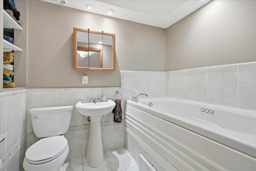 Upper-level bathroom offers a relaxing retreat with a large jetted soaking tub, extensive tile surround, recessed lighting, and convenient built-in linen shelving for towels and everyday essentials.