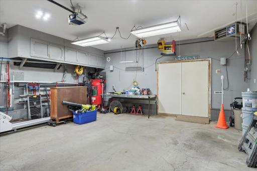 Oversized heated two-car garage offers exceptional space for vehicles, storage, and projects, featuring built-in overhead cabinetry, a permanent workbench that fold up against the wall. Shop through oversized double doors.