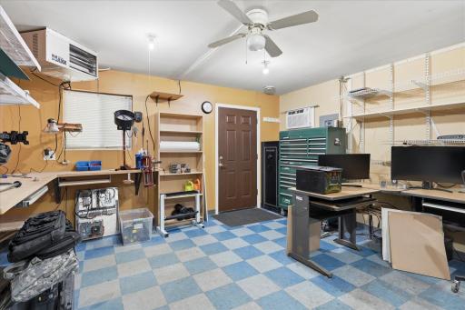 Versatile main-level office/ studio offers a comfortable workspace complete with heat and air conditioning, built-in work surfaces, abundant shelving, and plenty of room for multiple workstations or hobby space.
