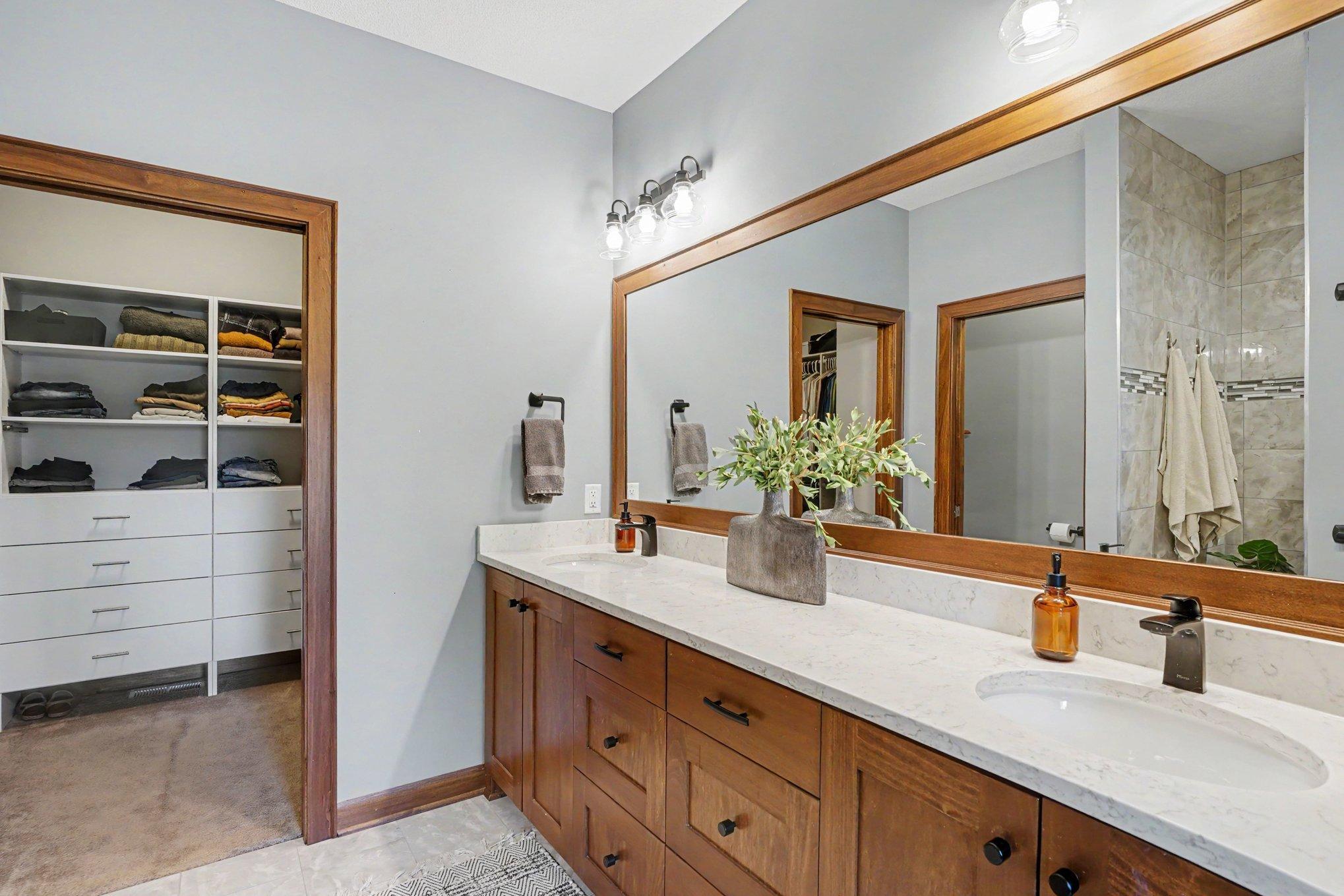 The primary bedroom attached bath has a framed mirror above the two sinks, new lighting and access to the custom walk-in closet with built-in drawers and shelving.