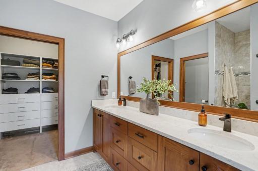 The primary bedroom attached bath has a framed mirror above the two sinks, new lighting and access to the custom walk-in closet with built-in drawers and shelving.