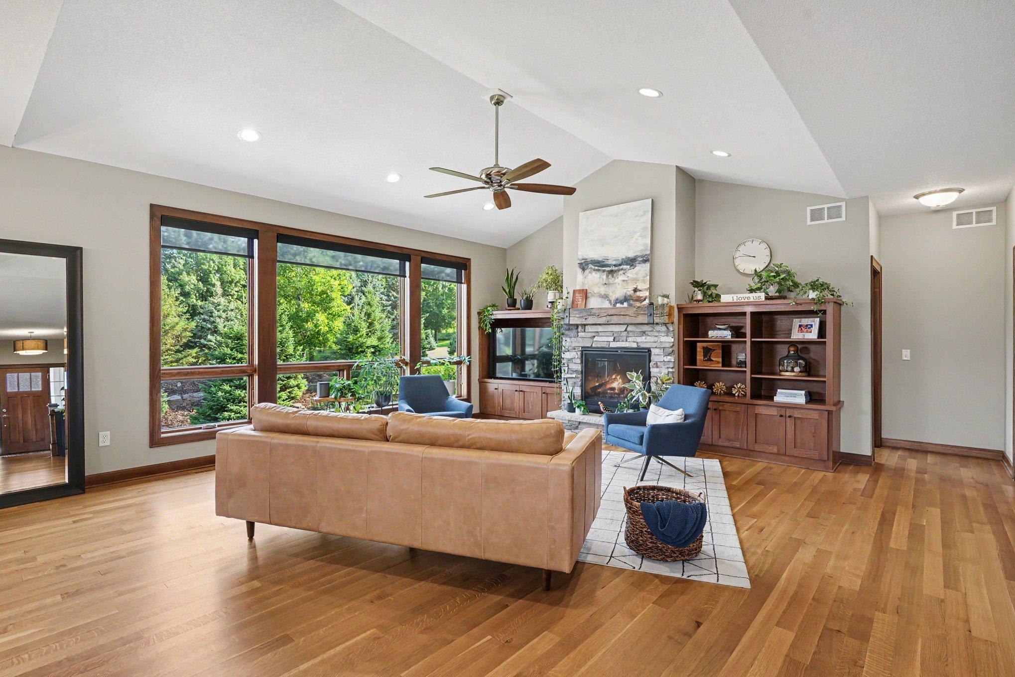 The living room has hardwood floors, a ceiling fan, recessed lighting and built-in bookshelves adorned on each side of the stone gas fireplace.