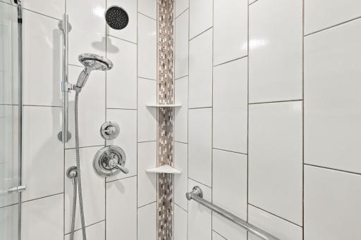 The glass-enclosed shower is designed with multiple fixtures and built-in storage.