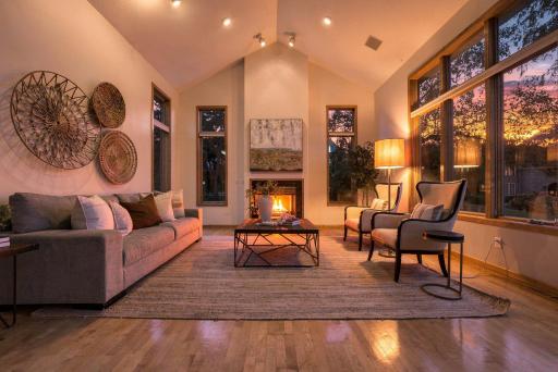 Vaulted ceilings, warm hardwood floors, and walls of windows create a beautiful living space filled with natural light, while the fireplace adds warmth and character as the sun sets outside.