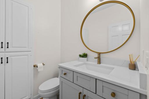 Spa-inspired bathroom with a sleek floating vanity, quartz countertop, gold fixtures, and a stunning round mirror as the centerpiece.