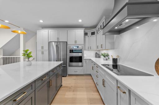 Full kitchen view showcasing the custom gray cabinetry, stone countertops, stainless steel appliances, and generous prep space throughout.