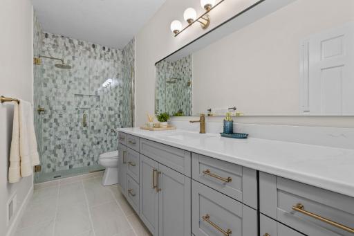 Lower level full bathroom with a beautifully tiled walk-in shower, dual vanity, gold fixtures, and designer tile work throughout.