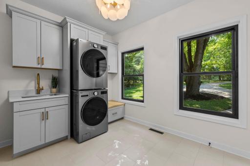 Convenient main-level laundry with a stacked washer and dryer, custom cabinetry, and a bright window overlooking the lush backyard.
