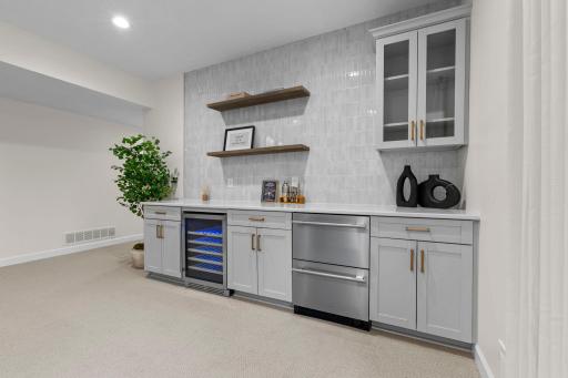 Full lower level bar with a wine fridge, stainless steel appliances, custom shelving, ice maker and a polished finish that rivals any upscale entertainment space.