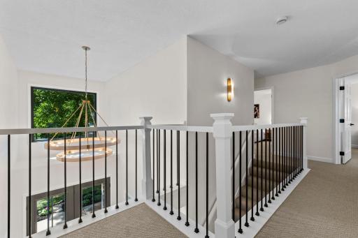 Open upper landing with beautiful iron railing detail, natural light pouring in, and views down to the main living area below.
