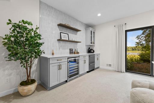 Lower level wet bar with custom cabinetry, open shelving, a beverage fridge, and a bright window view. The perfect spot for hosting.