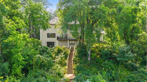 Breathtaking rear exterior view nestled among mature trees with a private wooded setting, stairway to the lake, and lush natural surroundings that make this property truly one of a kind.