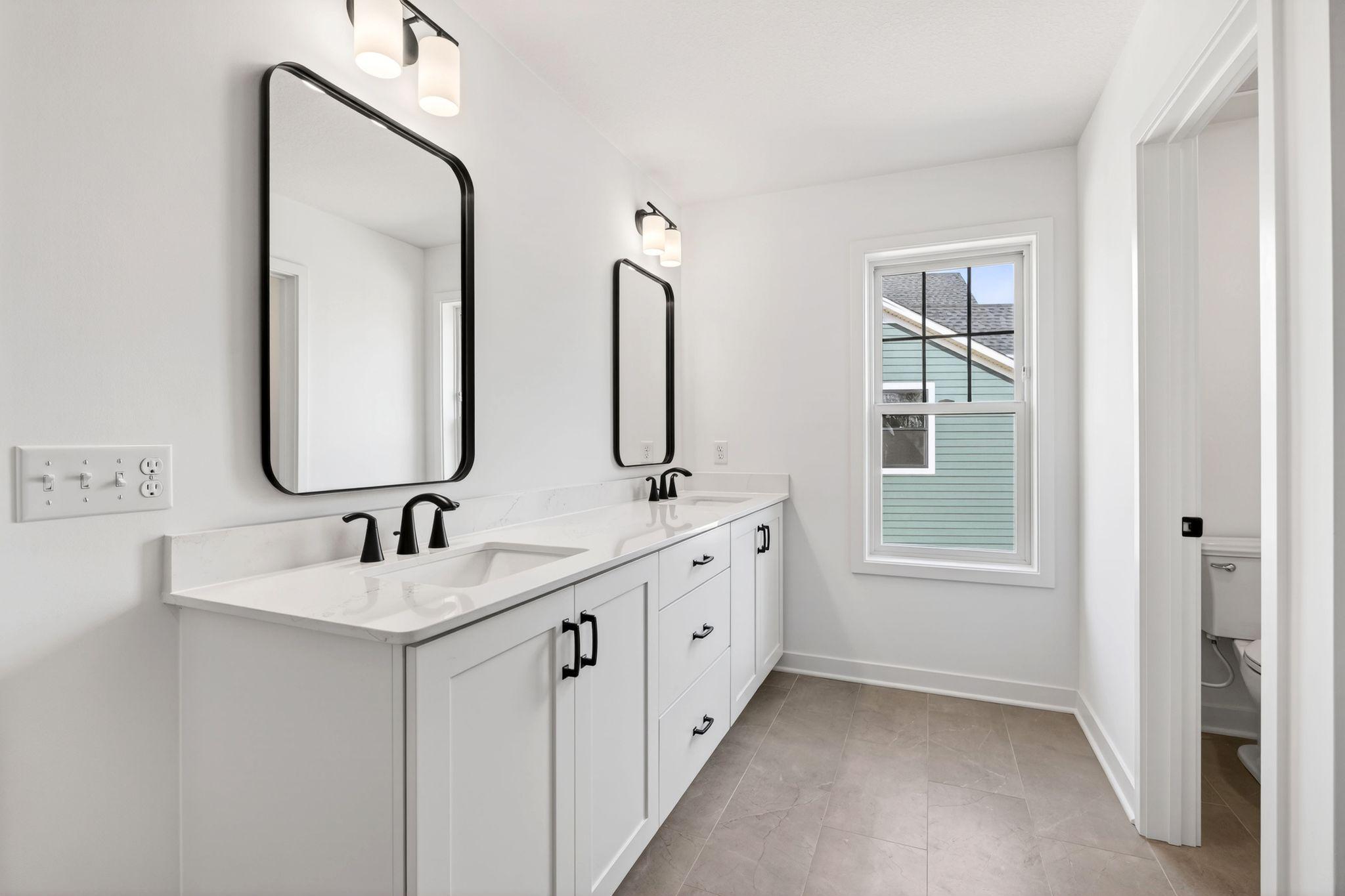 (Photo of a similar home, actual finishes may vary) Double sinks, Moen® brushed-nickel faucets and quartz countertops gleam in the owner’s suite bathroom