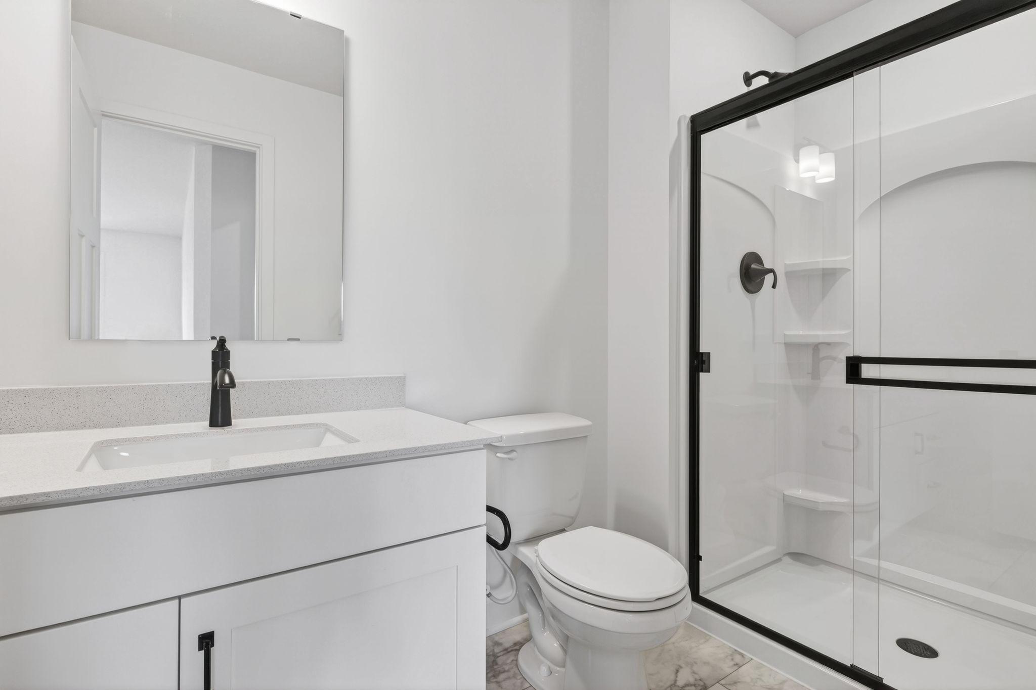(Photo of a similar home, actual finishes may vary) A private bathroom offers a shower with built-in shelves and a quartz-topped vanity with a Moen® chrome-finish faucet