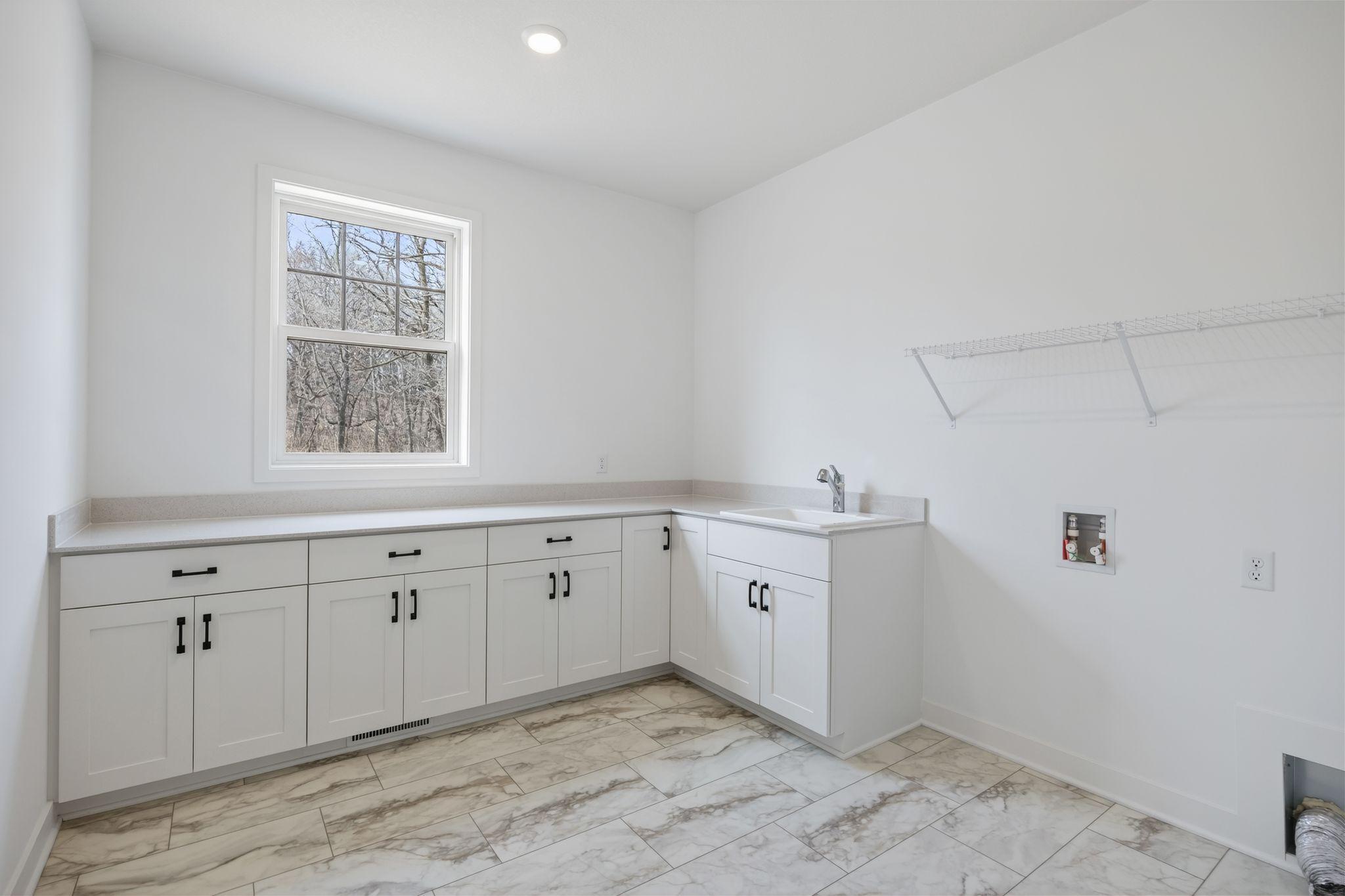 (Photo of a similar home, actual finishes may vary) Situated in a discreet corner on the first floor, this large laundry room provides ample space to complete daily household chores and other organizational tasks.