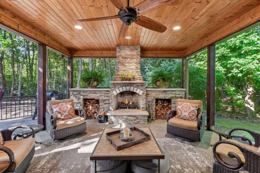 A stunning three-season porch with stone fireplace creates an unforgettable wooded retreat.
