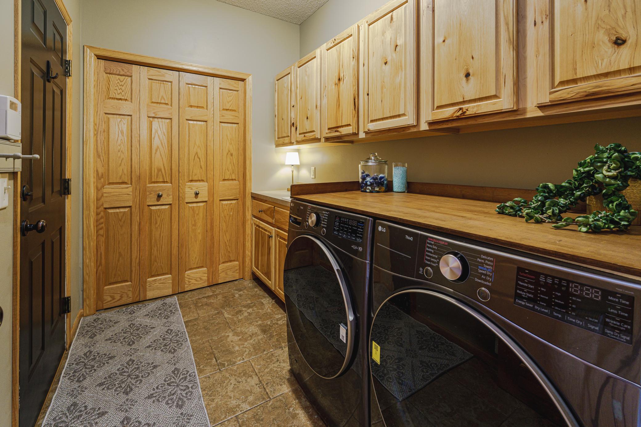 Adjacent to the powder bath is the laundry room, with tile flooring, a utility sink, folding counter, and newer washer and dryer.
