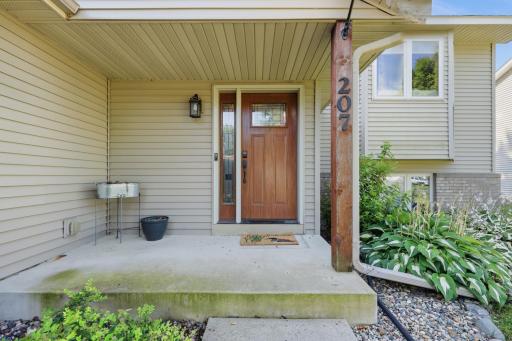 A rich wood-tone entry door with sidelight glass and a covered porch sets a warm, inviting tone at 207.