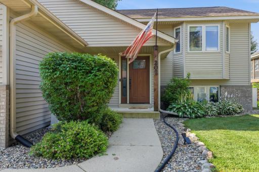 A tidy concrete walkway winds through rock-bed landscaping and lush greenery to the covered front entry. Mature shrubs and perennial plantings add texture and privacy to this welcoming approach.