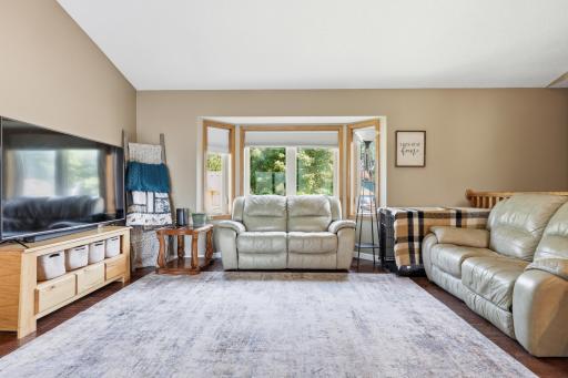 A picturesque bay window framed in warm wood trim anchors this vaulted living room, bringing in tree-lined views and plenty of natural light. Durable hardwood floors and a functional layout make everyday living easy here.