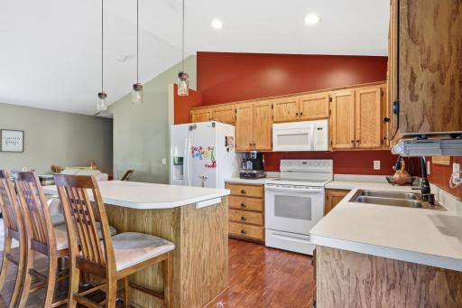 Full-height oak cabinetry offers generous storage, while updated pendant lighting brightens the workspace over the center island. The open sightline into the adjoining living area keeps the whole main level feeling connected.