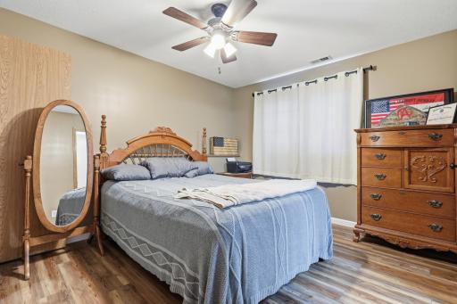 Located on the lower level, this spacious bedroom features warm wood-tone flooring, a ceiling fan, and an elegant wood bed frame. Neutral walls and ample closet space make it a versatile retreat.
