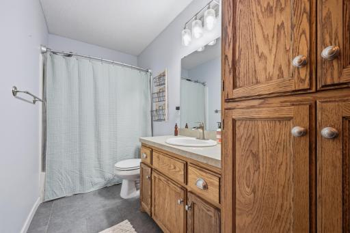 This full bathroom features a tub/shower combo, updated vanity lighting, and durable tile flooring. Rich oak cabinetry offers plenty of storage for everyday essentials.