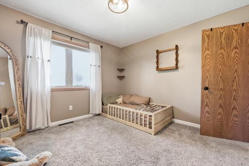 This second angle highlights the room's cozy layout, with a barn-style door and built-in corner shelving adding character. Soft carpet and a large window keep the space bright and comfortable.
