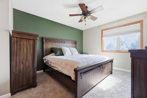 The primary bedroom features a designer green accent wall. Plush carpet and a large window bring in plenty of natural light.