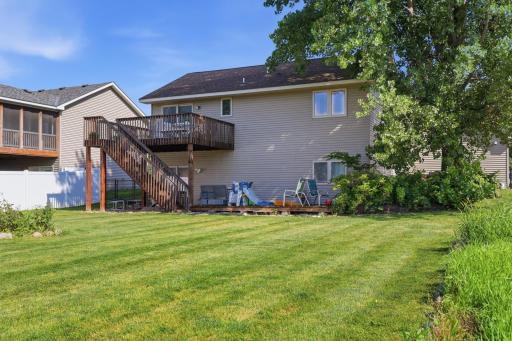 The elevated deck creates a private outdoor retreat above, while the lower patio area is perfect for kids' play equipment or additional seating. Mature trees offer welcome shade throughout the yard.
