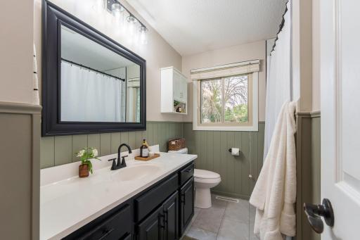 Beautifully remodeled bathroom, completed in 2025, featuring a tiled shower, wainscoting detail, new flooring, updated vanity, & fixtures.