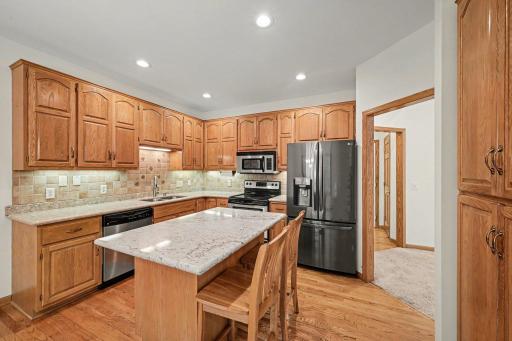 Kitchen with stainless steel appliances, center island seating, pantry, hardwood floors, and updated countertops.