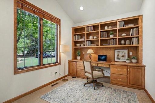 Main-level den/flex room with a wall of built-ins, natural light, and home office potential. Virtually staged.