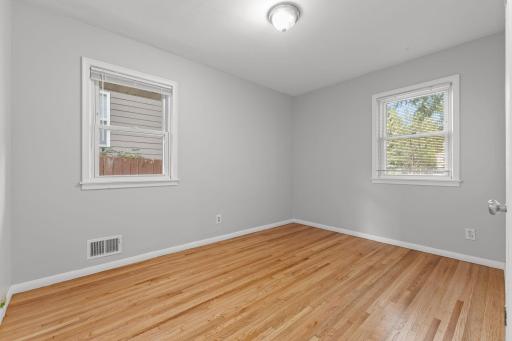Main-level bedroom with hardwood floors, neutral walls, and bright windows.
