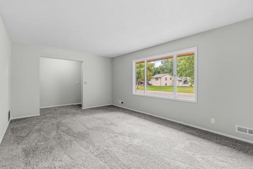 Spacious, light-filled living area with neutral finishes, plush carpeting, and a large picture window offering abundant natural light. Generous layout provides plenty of room for comfortable seating and entertaining.