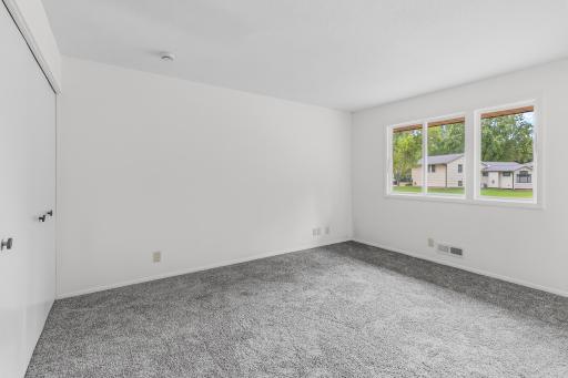 Spacious, light-filled bedroom featuring fresh neutral finishes, plush carpeting, generous closet space and a large window overlooking the neighborhood.