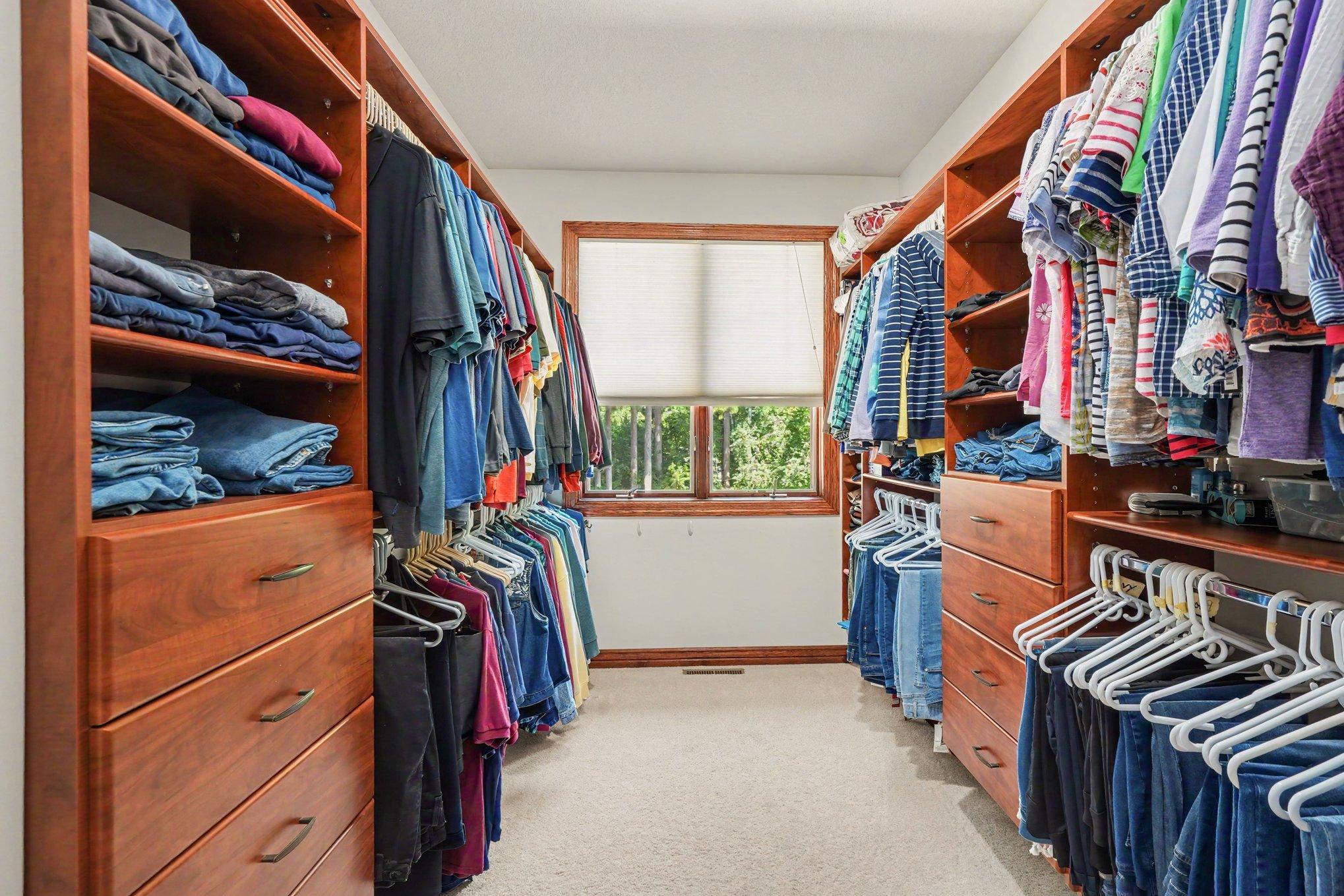 A spacious walk-in closet features extensive built-in shelving, drawers and hanging space to keep everything beautifully organized. A window at the end brings in natural light, making the space feel bright and functional.